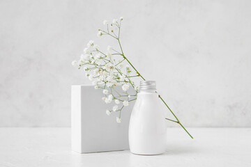 Bottle of cosmetic product, plaster podium and gypsophila flowers on light background