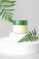 Composition with jar of cosmetic product, plaster podiums and fern leaves on light background