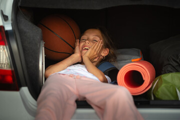 Happy girl lies in the trunk of a car among travel items