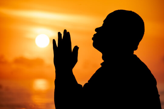 An evocative image of a man's silhouette, his hands outstretched to the heavens, as he stands in awe and reverence of Jesus during the resplendent sunset of the solstice.