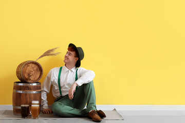 Young man in traditional German clothes with beer sitting near yellow wall