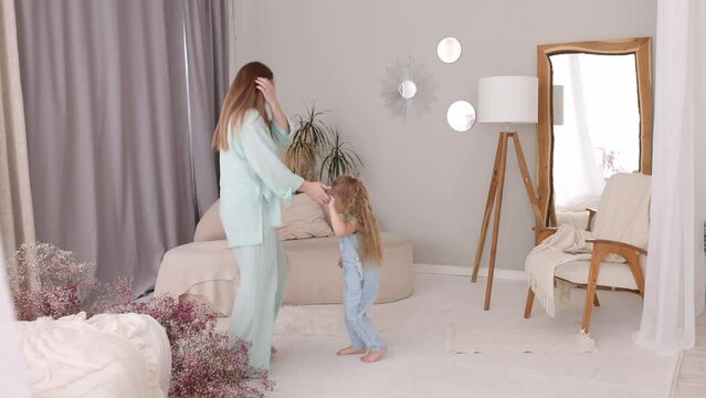 Active young mom babysiter and cute little kid daughter jumping dancing in modern house living room, happy family mother with child girl having fun enjoy playing funny activity together at home. 
