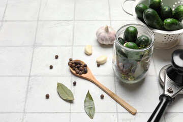 Jar and colander with fresh cucumbers for preservation on white tile background
