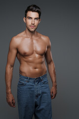 Sexy and charismatic brunette male model with a bare torso and jeans, against a gray background