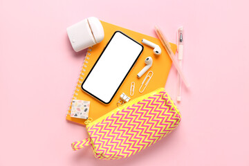 Stationery with mobile phone and earphones on pink background