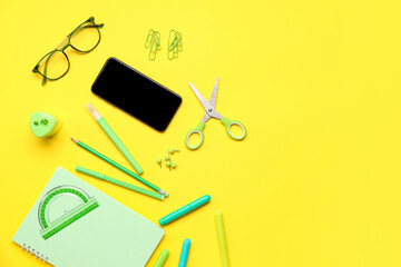 Mobile phone with eyeglasses and different stationery on yellow background