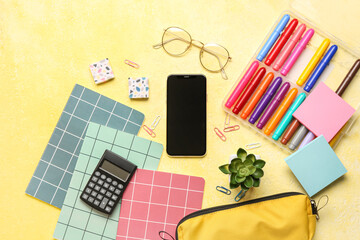Mobile phone with eyeglasses and different stationery on grunge yellow background