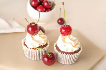 Board with tasty cherry cupcakes on light background