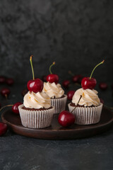 Plate with tasty cherry cupcakes on black background