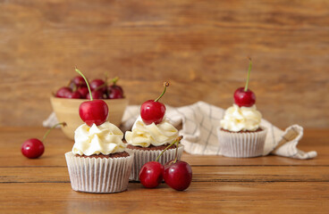 Tasty cherry cupcakes on wooden background
