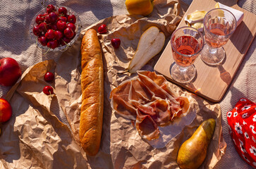 picnic in nature on a sunny summer day, rose wine in a glasses, fruits and food on a blanket