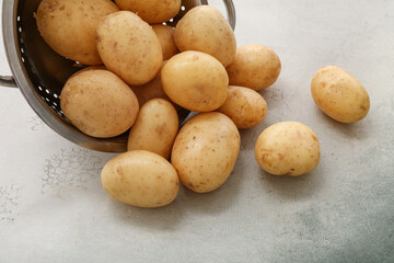 Colander with raw potatoes on white background
