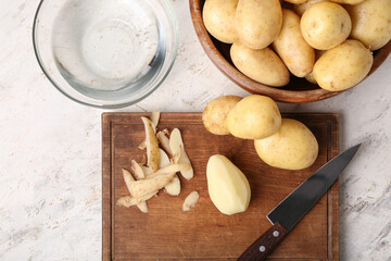 Fototapeta na wymiar Wooden board and bowl with raw potatoes on white background