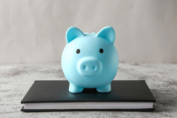 Piggy bank with book on grunge grey table near wall