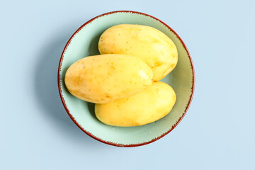 Bowl with raw potatoes on blue background