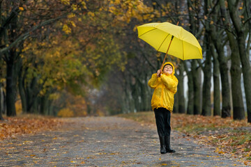 Obraz premium Happy childis jumping in the park in a yellow raincoat with an umbrella. Autumn rainy day