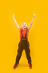 Full-length portrait of white-haired caucasian boy in work clothes and red T-shirt pointing fingers upwards. Vertical frame.