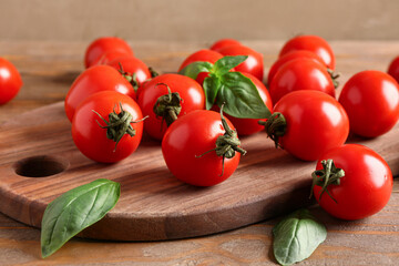 Board with fresh cherry tomatoes and basil on wooden table, closeup