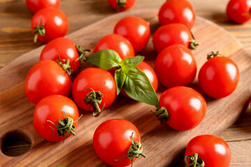 Board with fresh cherry tomatoes and basil on wooden table, closeup