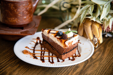 A Piece of Caramel Cheese Cake with white plate Topeed with Caramel and Chocolate on wooden table