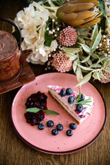 A Picece of Blue Berry Cheese Cake topped with Fresh Blue Berry and Blue Berry Jam with Tea pot on Wooden Table