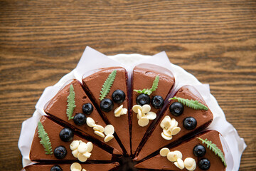 Top close up view of a chocolate cakes toppped with fresh Bluberry and white nuts with green leafs on wooden table background