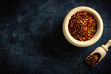 Top view red dried crushed hot chili peppers and chili flakes or powder in wooden spoon and bowl on...