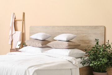 Comfortable bed with white pillows, bedside table and houseplant in bedroom