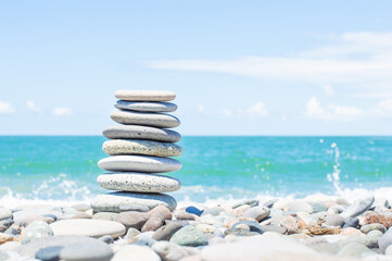 Pyramid stones balance on the beach next to the sea. Happy holidays. Pebble beach, calm sea, travel destination. Concept of happy vacation on the sea, meditation, spa, calmness.