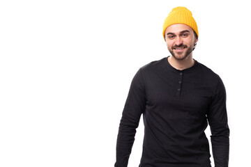 young brutal male model dressed in a black jacket and a yellow hat is smiling on a white background with copy space