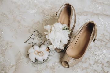 Fototapeta na wymiar details of the bride's clothes. gold wedding rings in a glass decorative box standing on cotton flowers. Wedding flower of the groom. Women's high-heeled shoes of golden color