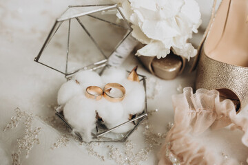 details of the bride's clothes. gold wedding rings in a glass decorative box standing on cotton flowers. Wedding flower of the groom. Women's high-heeled shoes of golden color