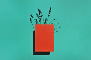 Orange book or notebook with lavender flowers inside on green background with long shadows....