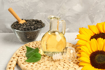 Sunflowers, seeds and decanter of oil on grey background