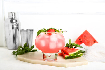 Board with glass of tasty watermelon cocktail, shakers and mint on white table
