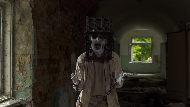 Ghost of maniac with cage on his head dragging dead body down corridor of asylum