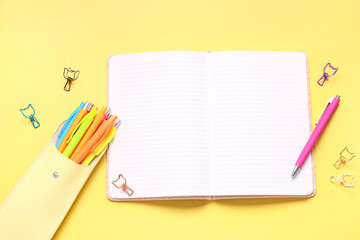 Case with colorful pens and blank notebook on yellow background