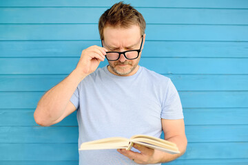 Portrait of mature man with big black eye glasses trying to read book but having difficulties...