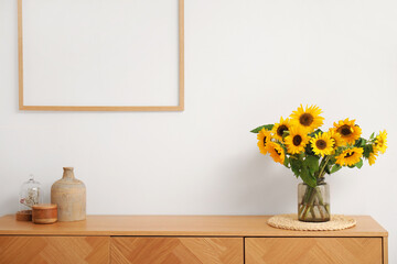 Vase with beautiful sunflowers on wooden cabinet near white wall, closeup