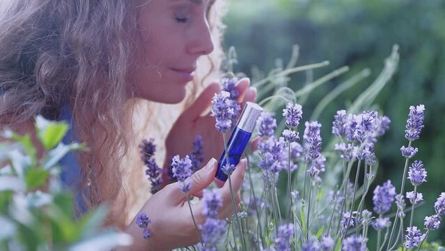 Beautiful girl sniffing roller shutter with aroma oils among greenery and lavender on a summer day. The concept of natural aromatic oils.
