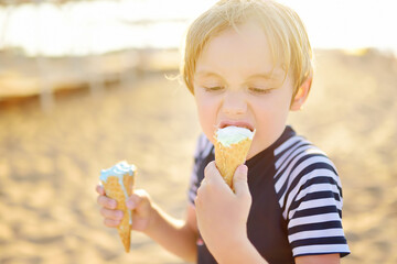 Preschooler boy eating ice cream on hot summer day on beach during family holiday.Gelato is loved...
