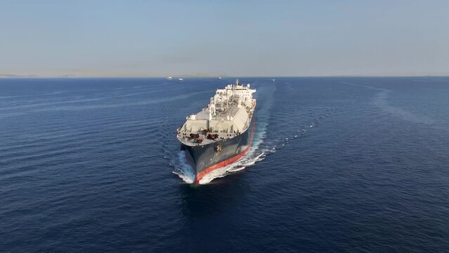 Panoramic aerial view of a big LNG tanker ship traveling with full speed over the ocean during sunset with copy space