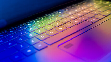 Laptop keyboard with vibrant hues illuminating the keys, wallpaper with colorful lights casting on...