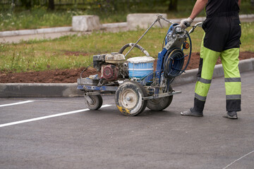 Construction of a parking lot for cars. A worker uses a special machine to mark parking lots with...