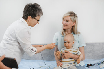 Child having hearing exam at otolaryngologist. Examining little patient, hearing test of infant kid by audiologist. Mother with baby visiting doctor for checkup