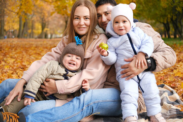 Parents and their little children twins spend time together in the autumn park sitting on a blanket