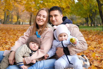 Family weekend. Parents and their little children twins spend time together in the autumn park sitting on a blanket