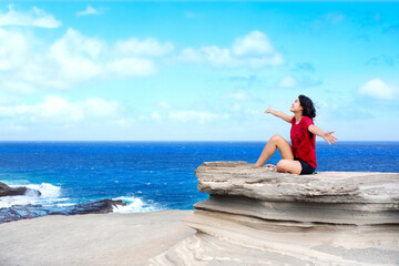 Young woman sitting on large rock cliff  by Hawaiian  ocean