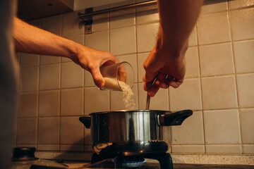 
man cooking in the kitchen concept pouring rice from a glass of new gender roles