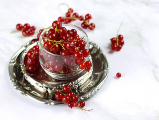 Red currant berries in a transparent bowl on a marble table, close up. Fresh red currants on light background with copy space. Atmospheric photo of ripe red currants in rustic style. Selective focus.
